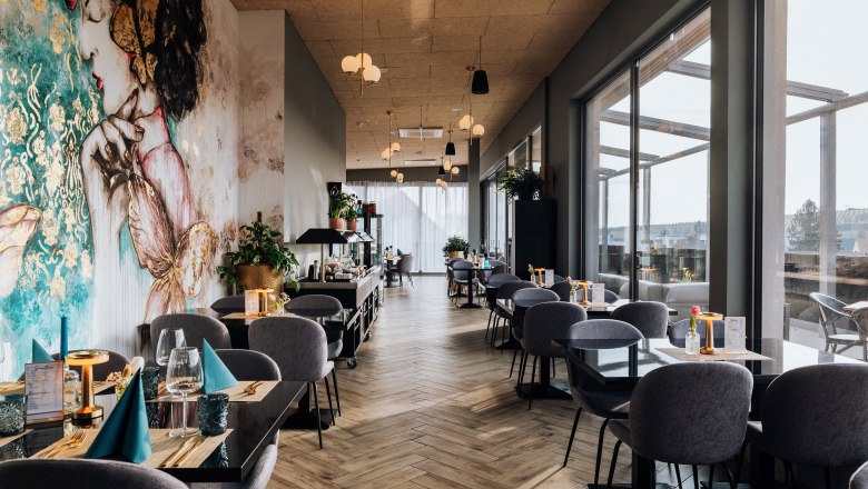 Roof Top Bar, © Bernhard Raab Innenansicht eines stilvollen Restaurants mit großen Fenstern und künstlerischer Wandmalerei.