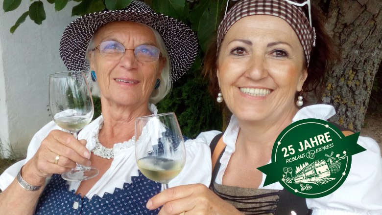 Weinviertler Lebensfreude, © Gritsch Zwei Frauen in traditioneller Kleidung stoßen mit Weingläsern an. Ein Logo mit der Aufschrift '25 Jahre Reblausexpress' ist eingeblendet.