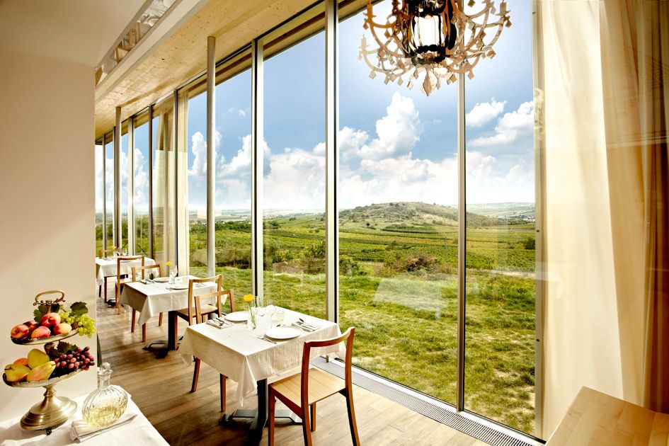 Innenansicht eines Restaurants mit großen Fenstern und Blick auf eine grüne Landschaft.