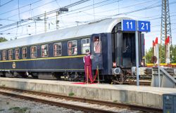 Mitarbeiter steht neben dem geöffneten Einstieg eines historischen Reisezugwagens am Bahnsteig.