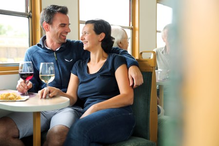 zwei Personen sitzen im Heurigenwaggon mit einem Glas Wein