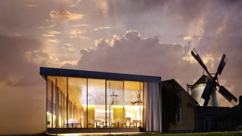 Moderne Glasarchitektur neben einer traditionellen Windmühle bei Sonnenuntergang.