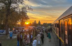 Gäste stehen bei Sonnenuntergang neben dem Reblaus Express auf einem Festgelände.