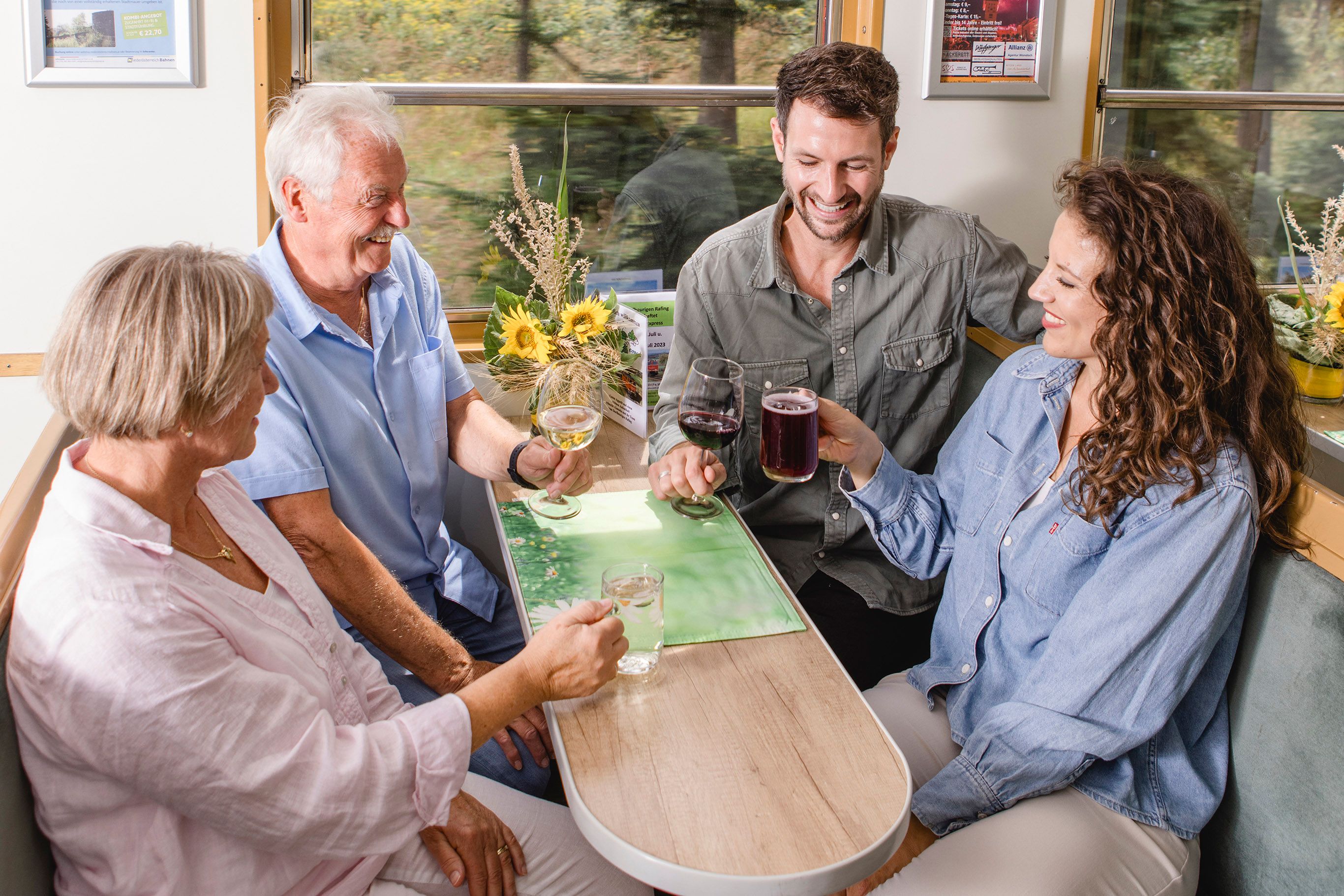 Vier Personen sitzen gemeinsam an einem Tisch im Heurigenwaggon des Reblaus Express und stoßen mit Wein, Traubensaft und Wasser an.