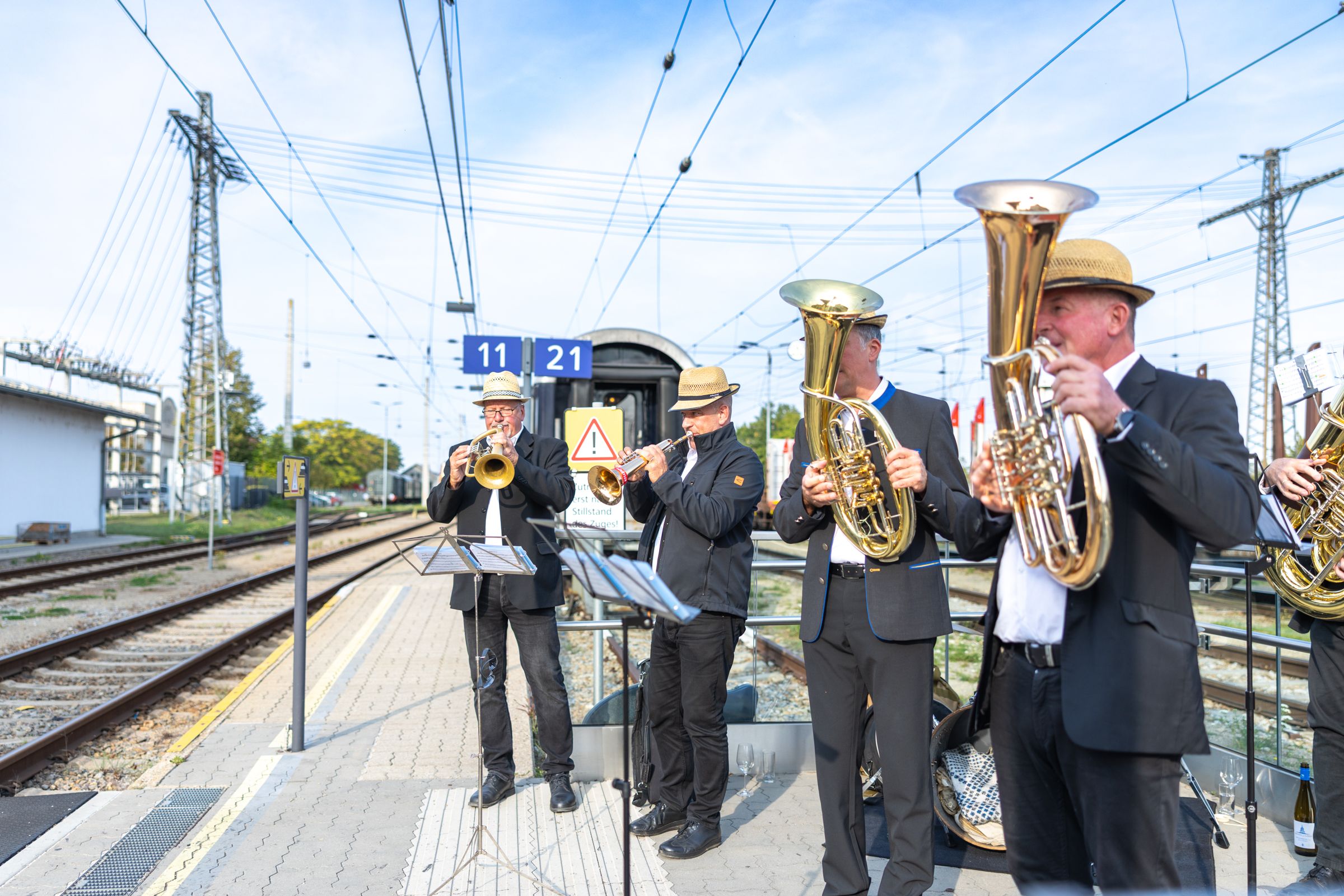 Vier Musiker spielen mit Trompete und Blasinstrumenten auf einem Bahnsteig.