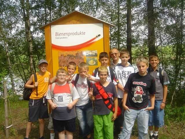 Gruppe von Jungen vor einem Schild mit der Aufschrift 'Bienenprodukte' im Freien.