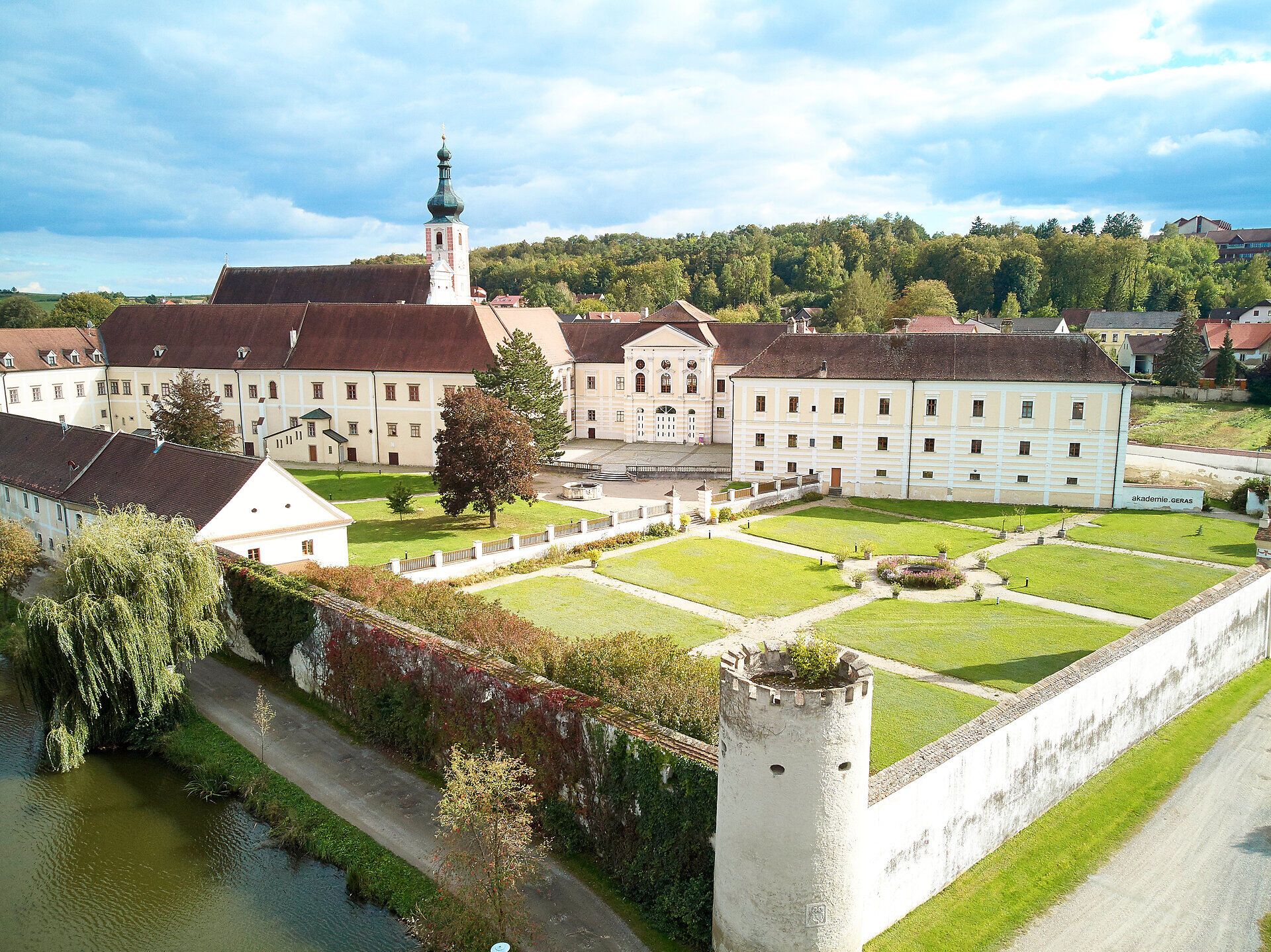 Luftaufnahme des Stifts Geras mit Garten und Turm im Vordergrund.