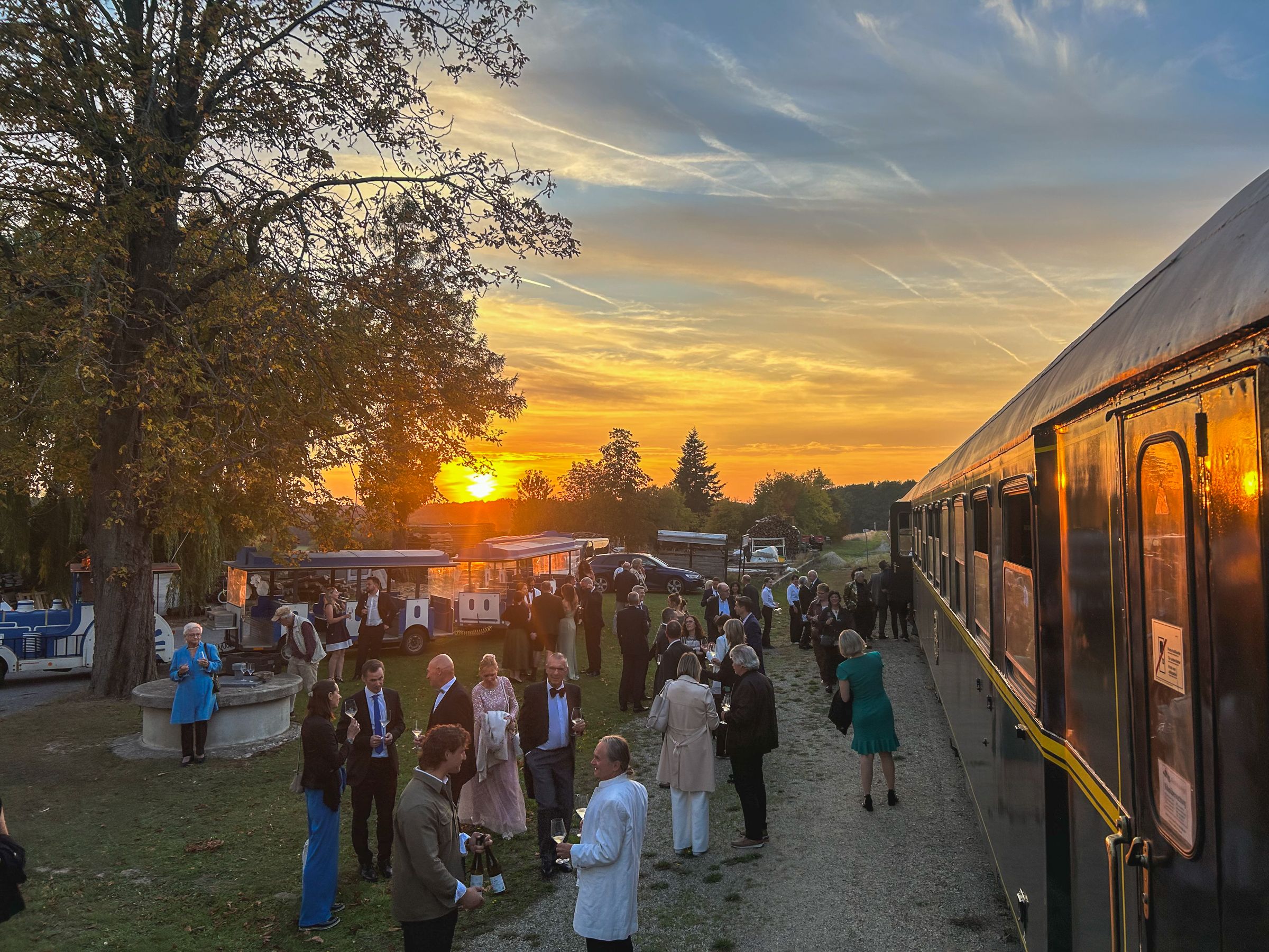 Gäste stehen bei Sonnenuntergang neben dem Reblaus Express auf einem Festgelände.