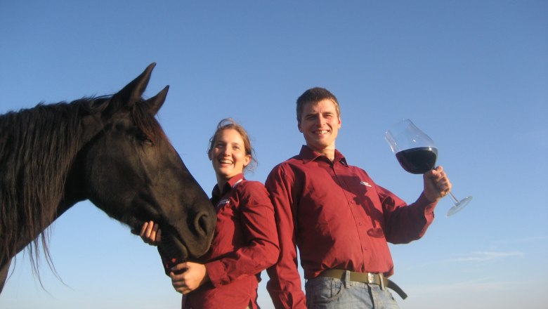 Two people in red shirts with a black horse and a large wine glass outside.