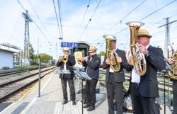 Vier Musiker spielen mit Trompete und Blasinstrumenten auf einem Bahnsteig.