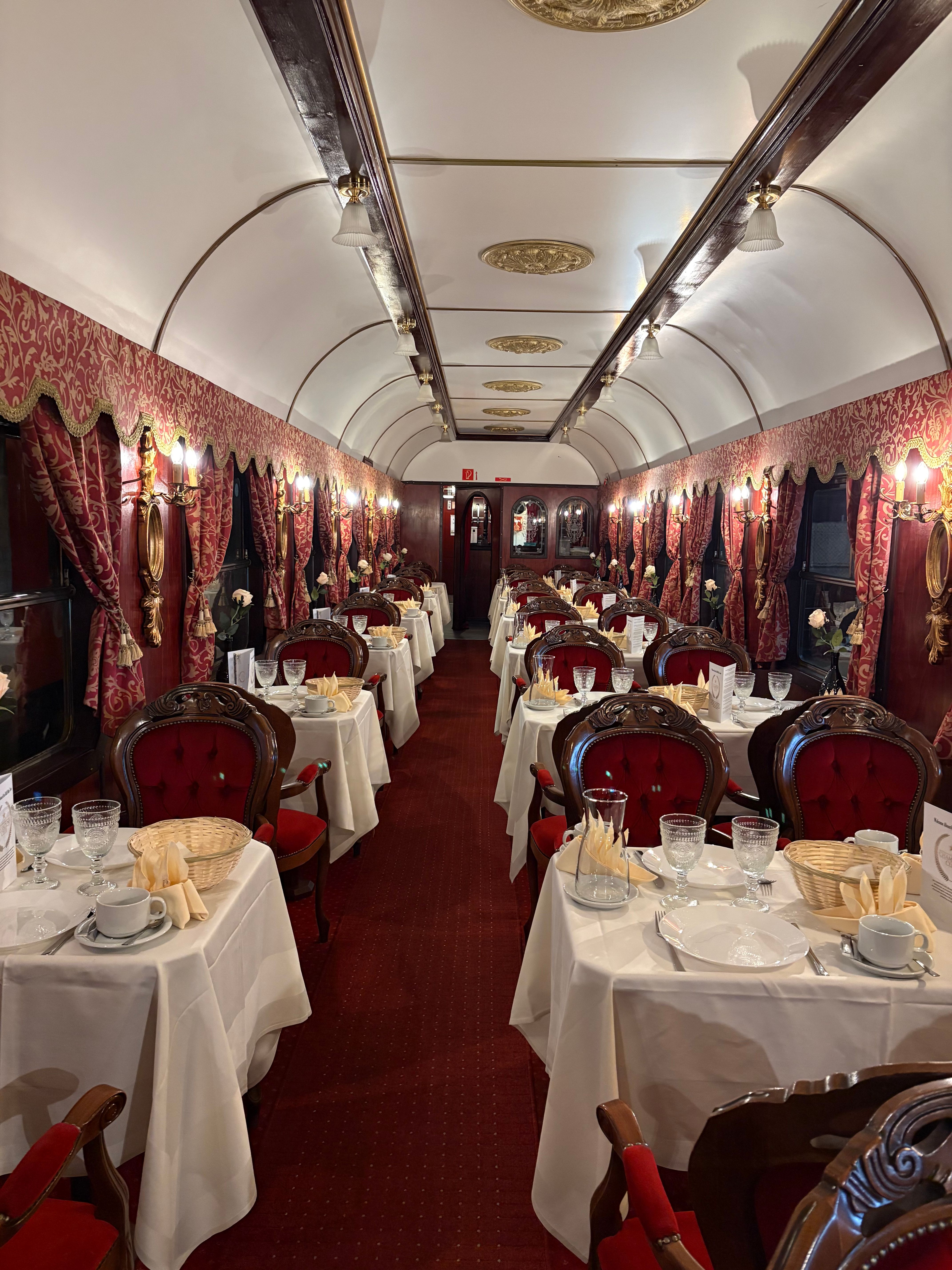 Eleganter Speisewagen mit roten Polstersesseln und gedeckten Tischen.