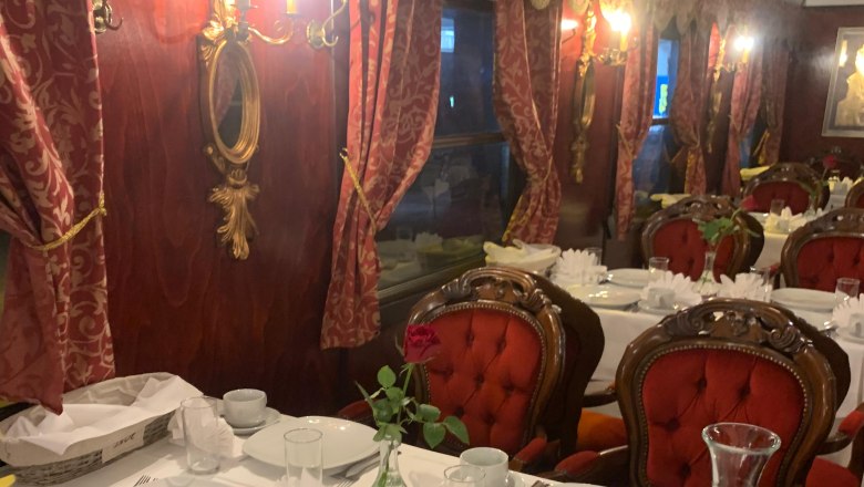 Elegantes Interieur eines Speisewagens mit roten Polstersesseln und gedecktem Tisch.