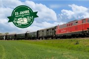 Roter Zug mit mehreren Waggons f&auml;hrt auf Gleisen durch eine gr&uuml;ne Landschaft unter blauem Himmel, daneben gr&uuml;nes Jubil&auml;umslogo