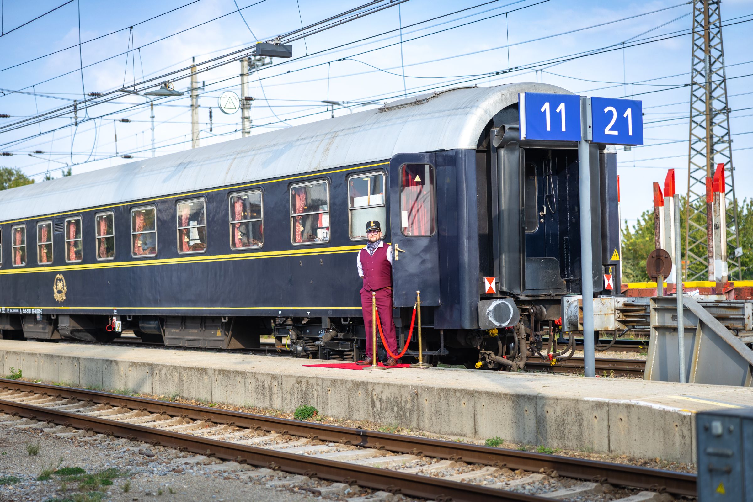 Mitarbeiter steht neben dem geöffneten Einstieg eines historischen Reisezugwagens am Bahnsteig.