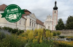Ein historisches Geb&auml;ude mit einem Turm im Hintergrund und einem Garten im Vordergrund.