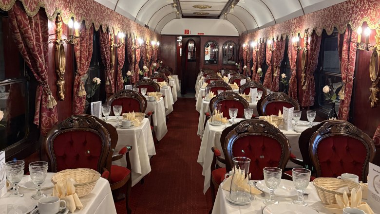 Eleganter Speisewagen mit roten Polstersesseln und gedeckten Tischen.