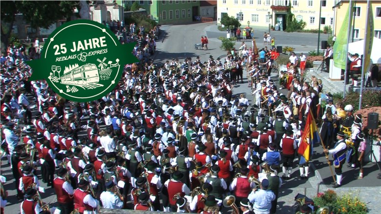 Eine gro&szlig;e Menschenmenge in traditioneller Kleidung feiert mit Musik und Fahnen.