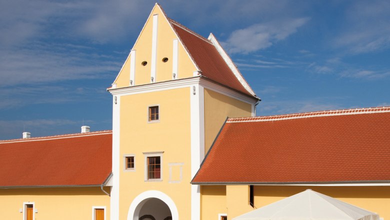 Gelbes Gebäude mit rotem Dach und Torbogen, blauer Himmel im Hintergrund.
